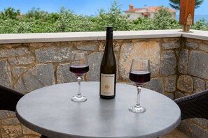 A stone wall with a bottle of wine and two glasses on a round table. - Pleades Seaside Caleano Gem in Mani, Near the Sea (Agios Nikolaos)
