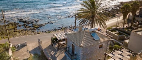 Een stenen gebouw met een balkon, een palmboom en uitzicht op de zee.