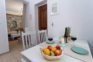 A dining area with a table set for two, featuring a fruit basket, two wine glasses, and a candle. - Pleades Seaside Caleano Gem in Mani, Near the Sea (Agios Nikolaos)
