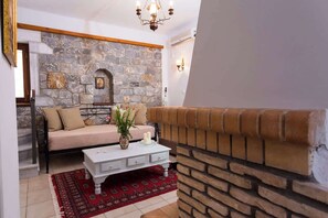 Ein gemütliches Wohnzimmer mit Kamin aus Stein, einer Couch, einem Couchtisch und einem roten Teppich mit Muster.
