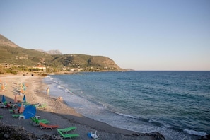 A beach with chairs and umbrellas, a clear sky, and mountains in the background. - Pleades Seaside Caleano Gem in Mani, Near the Sea (Agios Nikolaos)