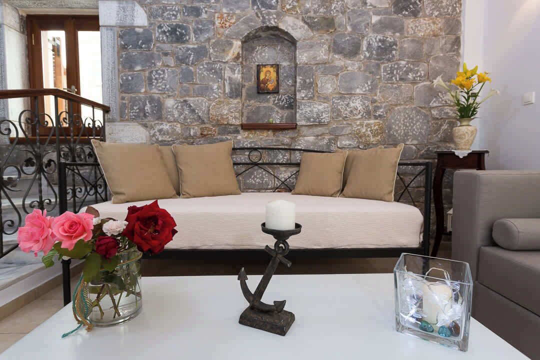 Un mur de pierres, un canapé avec des coussins, un vase rempli de fleurs, un chandelier et une table avec une bougie.