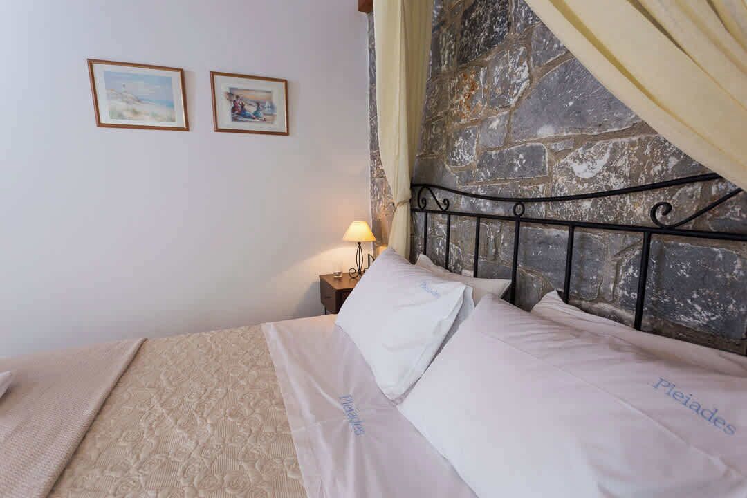 Una cama con sábanas blancas y una pared de piedra al fondo.