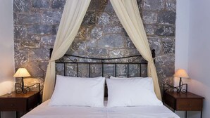 Een bed met een stenen achtergrond, twee bedlampen en een hemelbed.