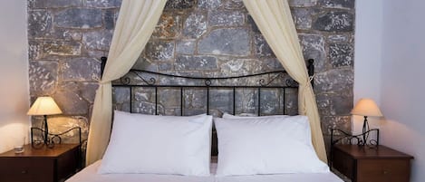 Een bed met een stenen achtergrond, twee bedlampen en een hemelbed.
