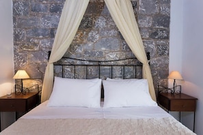 A bed with a stone wall backdrop, two bedside lamps, and a canopy. - Pleades Seaside Caleano Gem in Mani, Near the Sea (Agios Nikolaos)