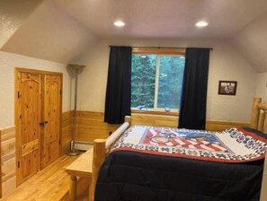 Una habitación con una cama, un armario de madera, una ventana con cortinas y vistas a árboles.
