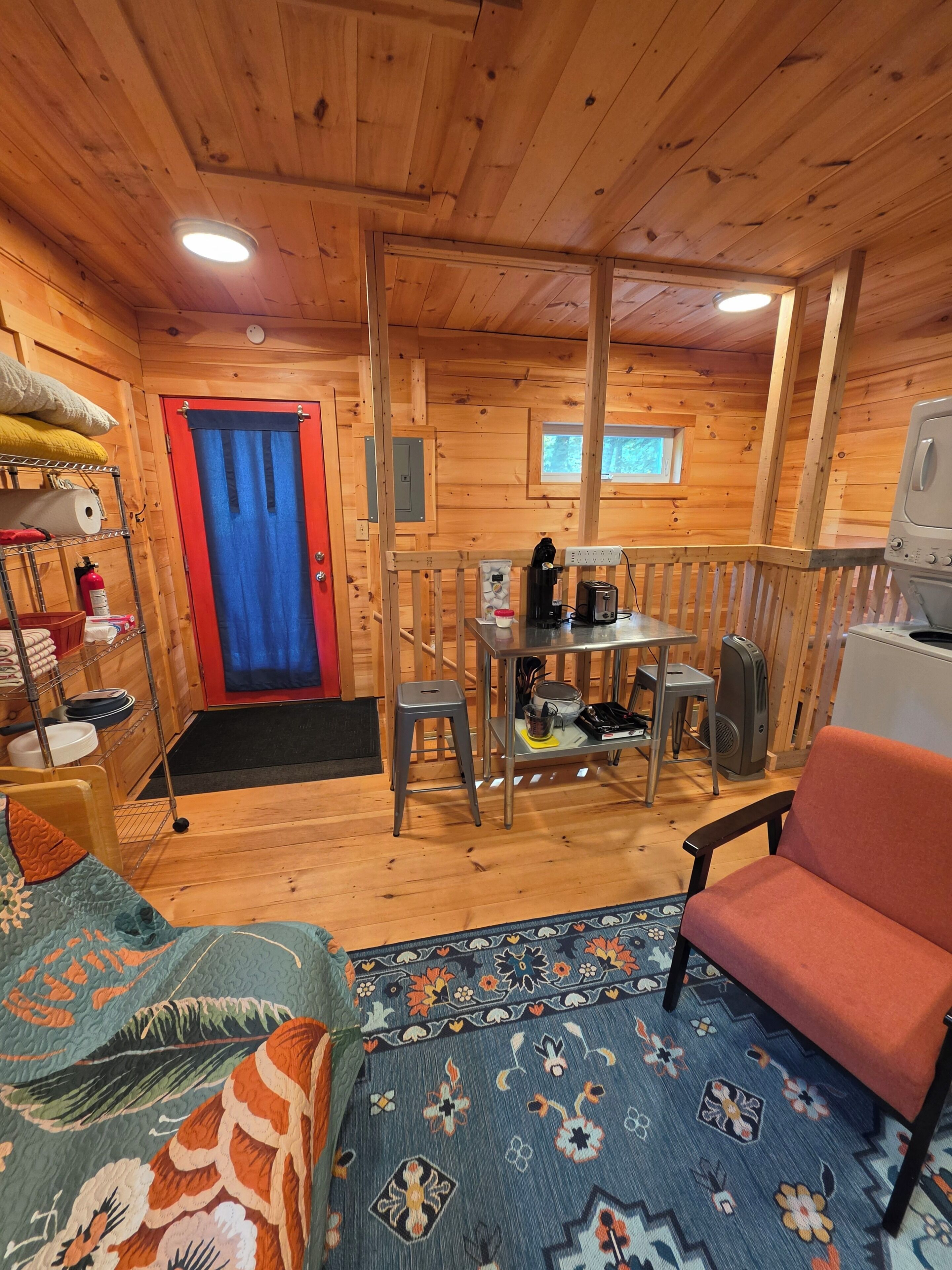 L’intérieur d’une cabane en bois comprend un lit, une table avec une chaise, une petite cuisine et une fenêtre.