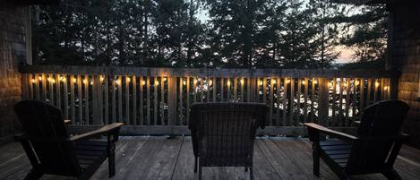 A wooden deck with two chairs and a table, surrounded by a wooden fence with string lights.