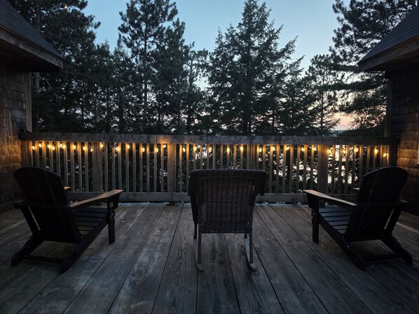 A wooden deck with two chairs and a table, surrounded by a wooden fence with string lights.