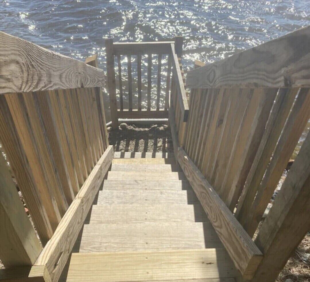 En trätrappa som leder ner till en strand, med ett räcke på båda sidor.
