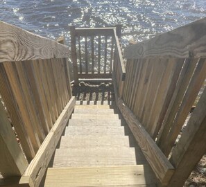 A wooden staircase leading to a beach with a railing on both sides. - Round Lake Cabin. Escape to lake life close to amenities and attractions. (Charlotte)
