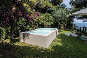 Una piscina rettangolare all'aperto con un bordo in vimini, circondata da vegetazione lussureggiante e piante fiorite.