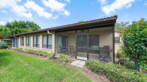 Ein Haus mit überdachter Terrasse, großen Fenstern und einem gepflegten Garten.