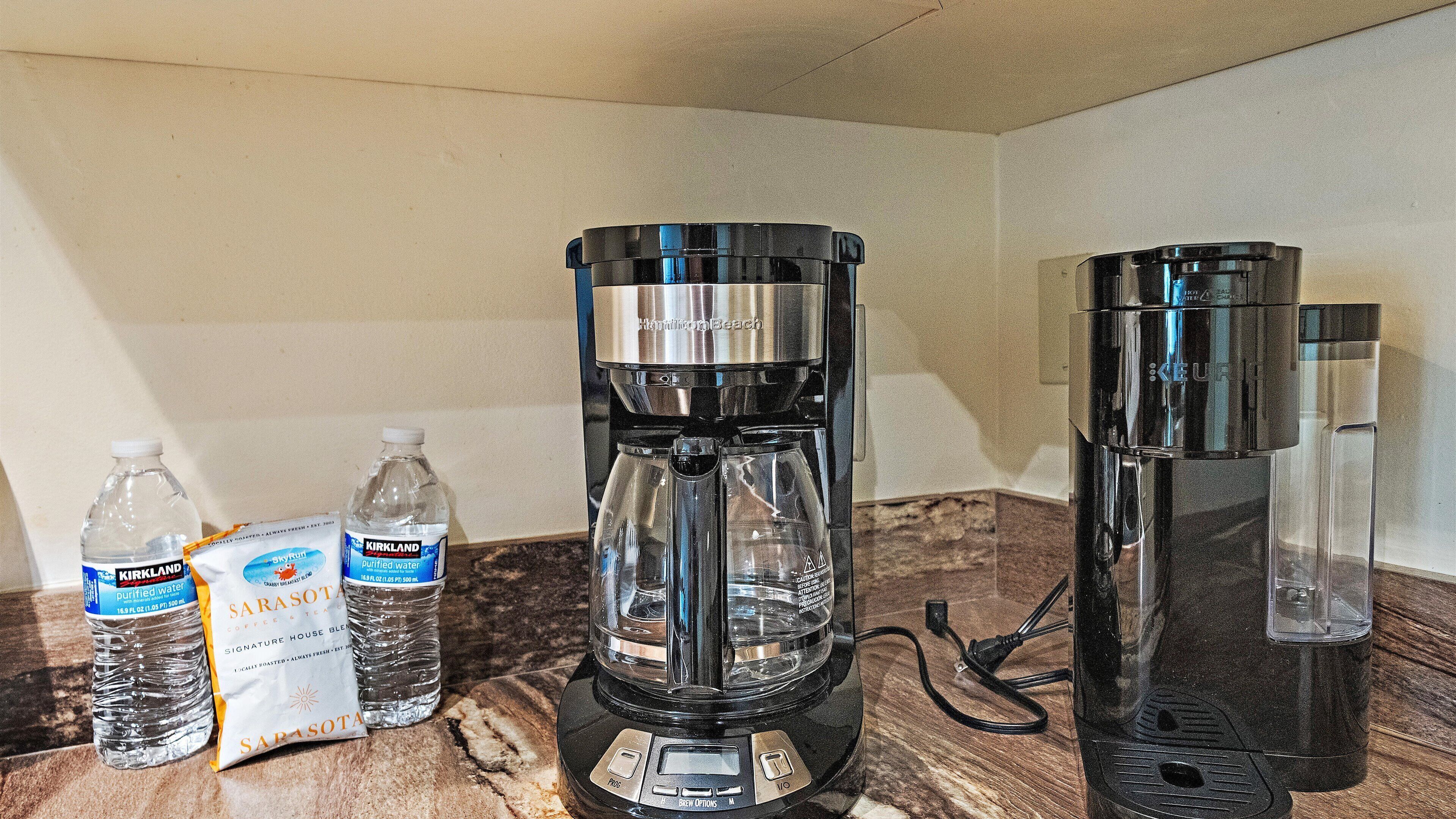 Eine Kaffeemaschine, zwei Wasserflaschen und ein Kaffeepäckchen auf einer Küchenarbeitsplatte.