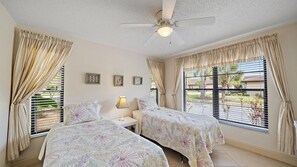 Ein Schlafzimmer mit zwei Betten, einem Deckenventilator und einem Fenster mit Jalousien.