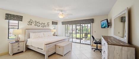 A bedroom with a bed, bedside tables, a desk, a chair, a TV, and a balcony with a view.