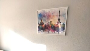 A white leather sofa with a plush cushion, a small plush toy, and a framed cityscape painting on the wall. - Comfortable apartment—5-minute walk to the RER An at Busy-Saint-Georges—8 minutes to Disney. (Bussy-Saint-Georges)