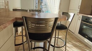 A kitchen with a central island, two chairs, a window with sheer curtains, and a built-in oven. - Comfortable apartment—5-minute walk to the RER An at Busy-Saint-Georges—8 minutes to Disney. (Bussy-Saint-Georges)