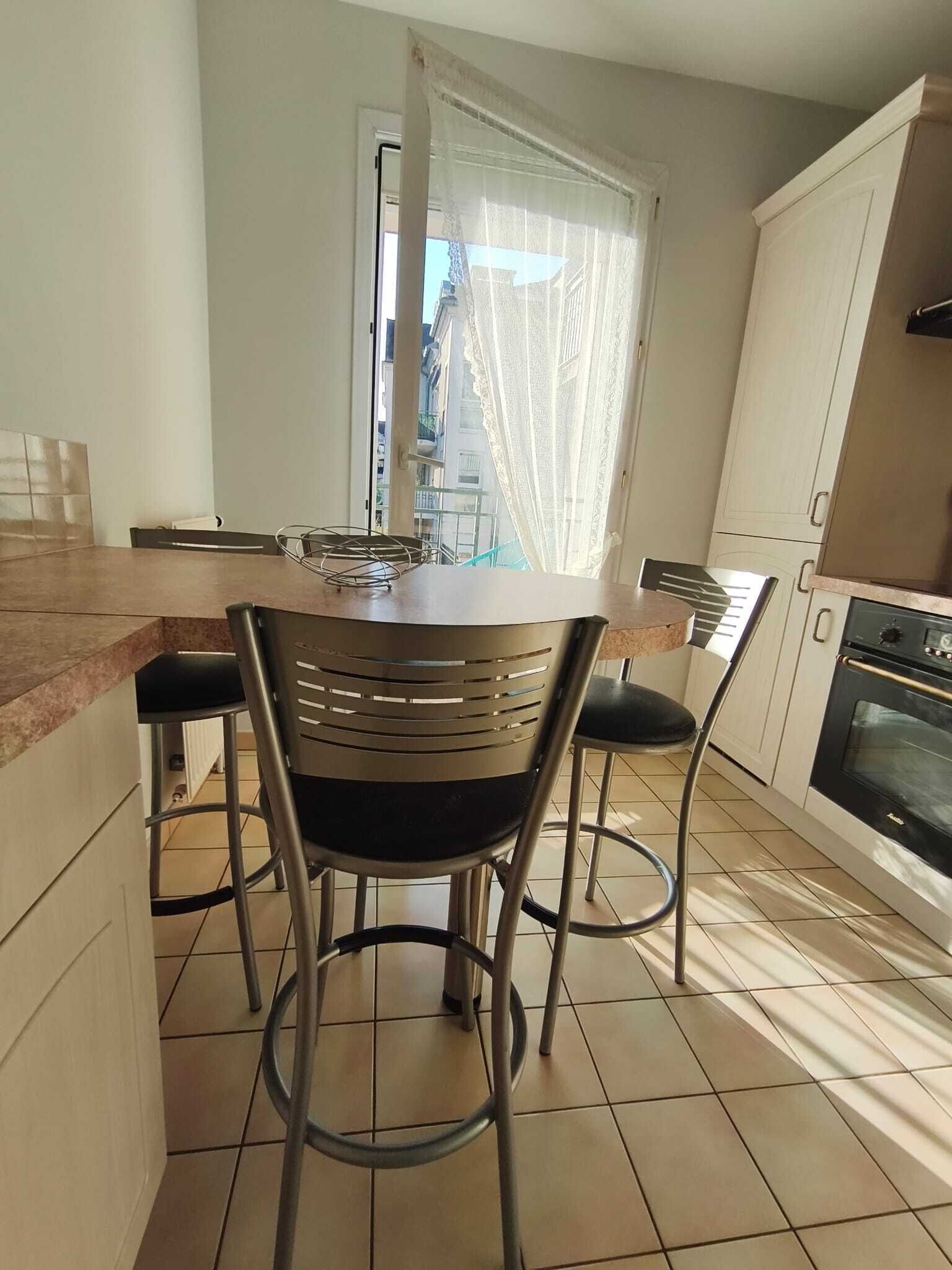 A kitchen with a central island, two chairs, a window with sheer curtains, and a built-in oven. - Comfortable apartment—5-minute walk to the RER An at Busy-Saint-Georges—8 minutes to Disney. (Bussy-Saint-Georges)