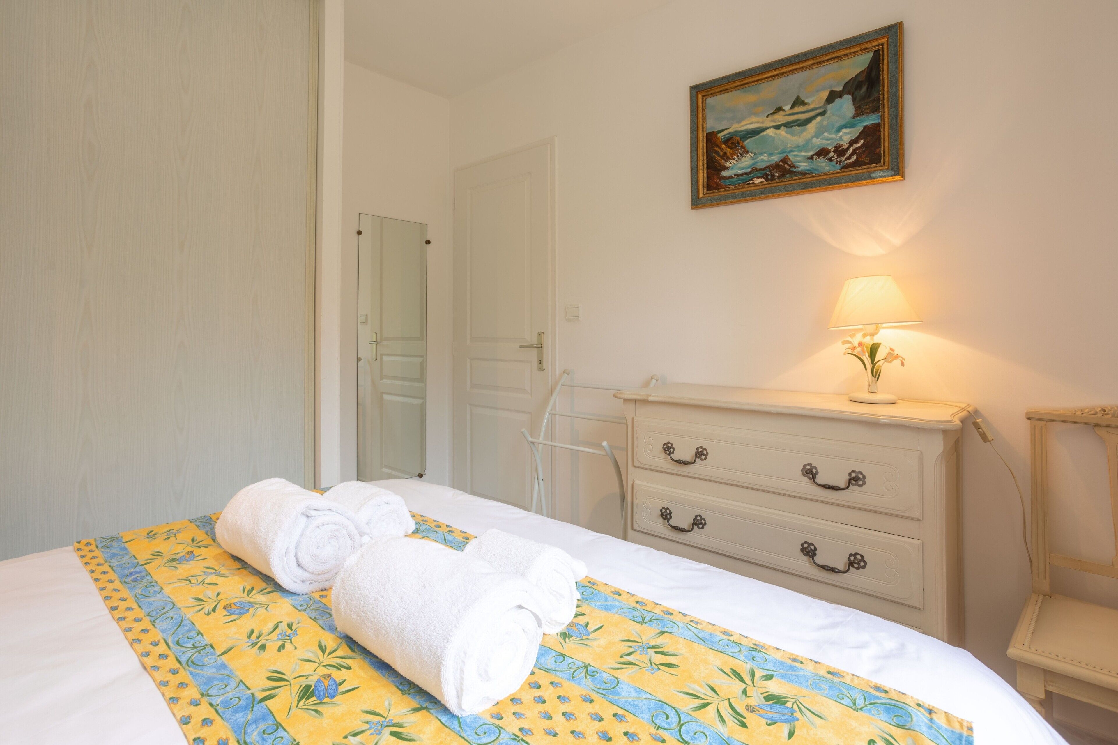 Ein Hotelzimmer mit Bett, Kommode, Lampe und einem Bild an der Wand.