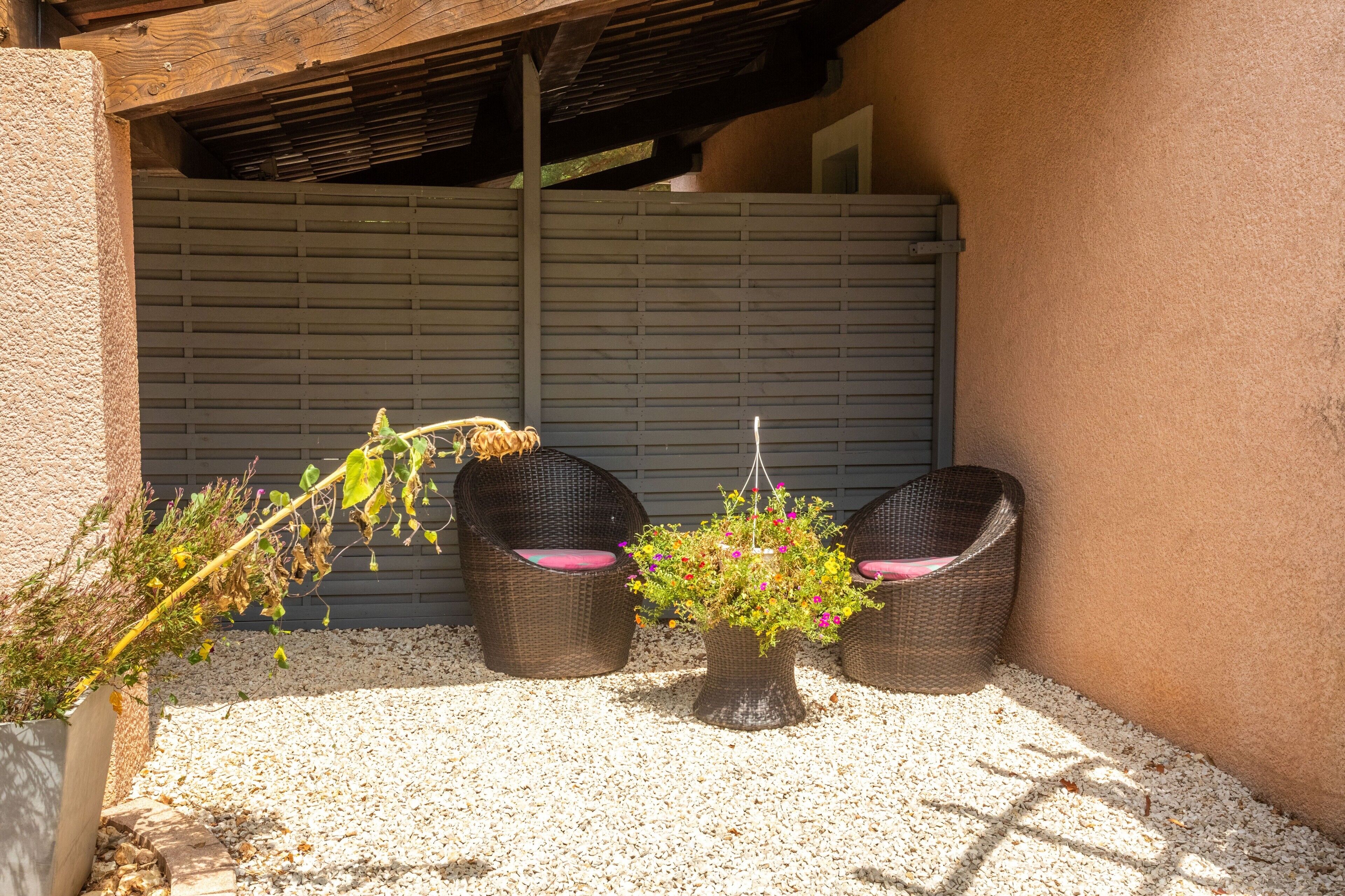 A covered outdoor seating area with two wicker chairs and a potted plant.