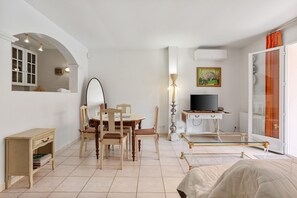 A well-lit room with a dining table, chairs, a TV, and a bed.