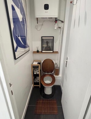 Ein kleines, kompaktes Badezimmer mit Toilette, einem gerahmten Bild an der Wand und einer kleinen Ablage für Pflegeprodukte.