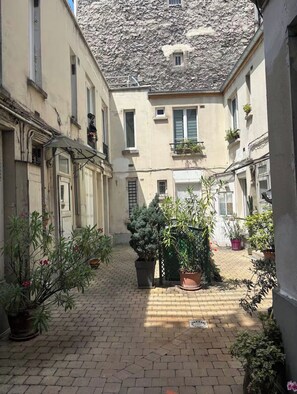 A narrow alleyway with buildings on either side, potted plants, and a cobblestone path. - Studio overlooking a flower-filled courtyard in the heart of Montmartre (Paris)