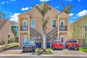 A multi-story residential building with a central staircase, parking spaces, and a palm tree in the middle. - Isla Bella - 2BR Steps from the Beach with Pool (South Padre Island)