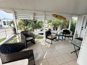 A covered outdoor seating area with wicker furniture and a pool in the background. - Family Friendly Resort Cottage with Private Patio (Port Isabel)