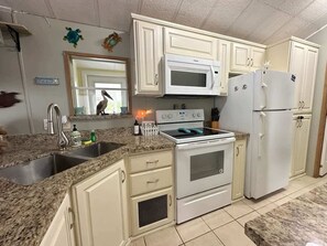 A kitchen with white cabinets, a microwave, a stove, and a refrigerator. - Family Friendly Resort Cottage with Private Patio (Port Isabel)