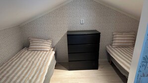 A small, single-room apartment with two beds, a black dresser, and a patterned wall.