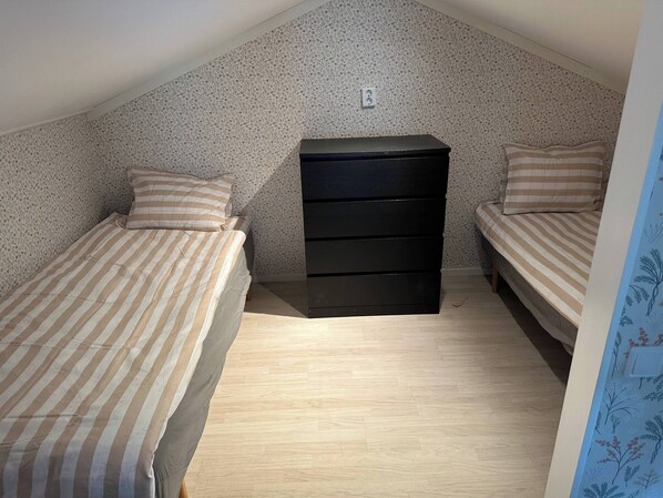 A small, single-room apartment with two beds, a black dresser, and a patterned wall.