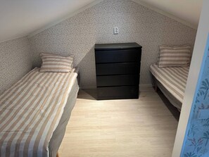 A small, single-room apartment with two beds, a black dresser, and a patterned wall. - Happy Stay Apartment (Vallda)