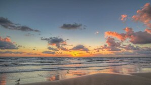 A beach with waves, a sunset, and scattered clouds.
