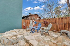 Une terrasse avec un sol en pierre, une clôture en bois et du mobilier d’extérieur comprenant des chaises et une table.