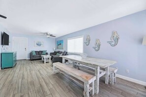 Una sala de estar con piso de madera, una mesa de comedor con bancos, un sofá y un televisor.