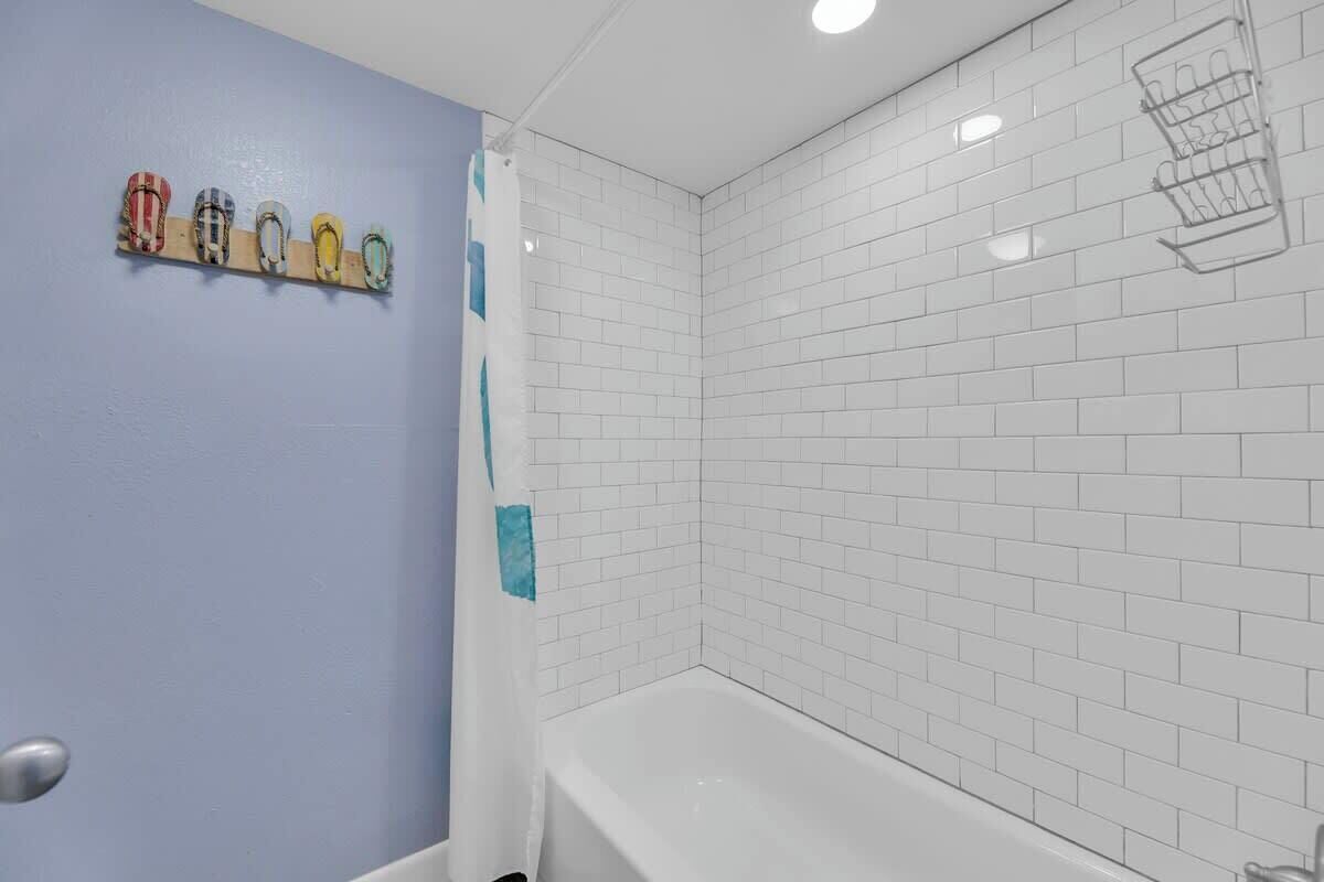 Een badkamer met witte betegelde wanden, een wit bad en een douchegordijn.