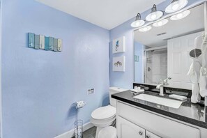 Un bagno con un WC bianco, un lavandino con piano in nero e uno specchio con illuminazione. Sono presenti porta asciugamani a parete e quadri incorniciati.