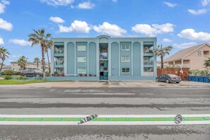 Un edificio de varios pisos con entrada central, balcones y un estacionamiento al frente.