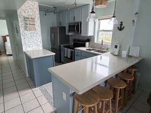 A modern kitchen with a central island, bar stools, a microwave, and a refrigerator.