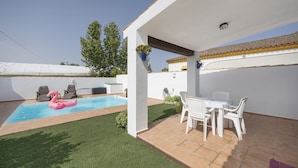 En overdækket terrasse med swimmingpool, udendørs møbler og et lille bord.
