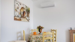En spiseplads med et bord dækket til to personer, en stol, en dekorativ vase og en vægmonteret aircondition.