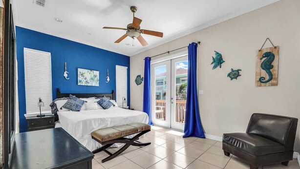 A bedroom with a bed, a desk, a chair, a ceiling fan, and a balcony with blue curtains. - Isla Bella - 2BR, Balcony & Pool, Beachfront Condo (South Padre Island)