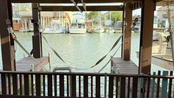 A view from a covered outdoor area with a hammock, wooden deck, and a view of boats on water.