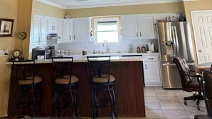 Una cocina con armarios blancos, un refrigerador de acero inoxidable, techo de madera y ventilador de techo.