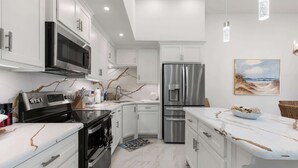 A modern kitchen with white cabinetry, stainless steel appliances, and a marble countertop. - Isla Bella - 2BR, Cielo del Sol Luxury Condo (South Padre Island)