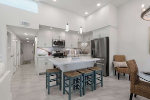 A modern kitchen with white cabinets, a central island with stools, a stainless steel refrigerator, and a microwave. - Isla Bella - 2BR, Cielo del Sol Luxury Condo (South Padre Island)