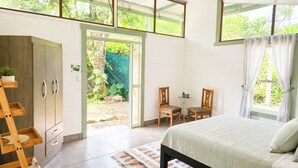 Ein Schlafzimmer mit einem Bett, einem Holzschrank, einem kleinen Tisch mit Stühlen und Blick auf den Garten durch eine Tür.